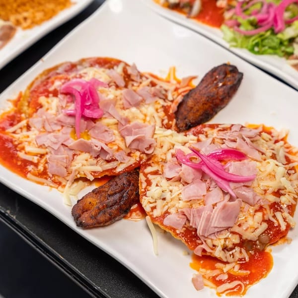 Two sopes topped with red sauce, cheese, ham, and pickled onions, with a fried plantain.