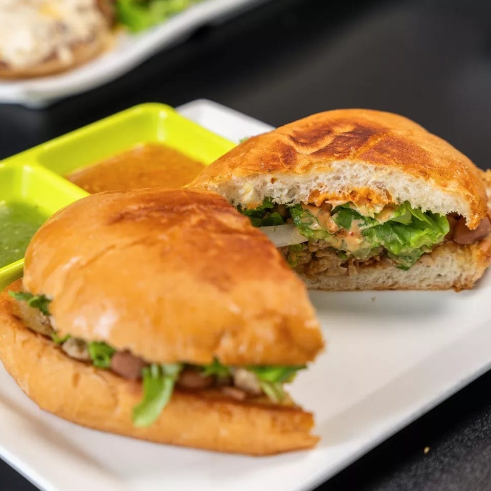 Two halves of a sandwich with lettuce, meat, and sauce, served with two dipping sauces.