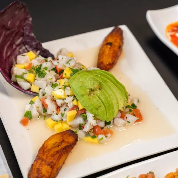 Ceviche with mango, avocado, and plantains on a white plate.