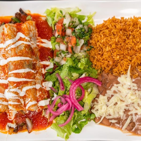 Enchiladas with red sauce and crema, served with rice, refried beans, and a side salad.