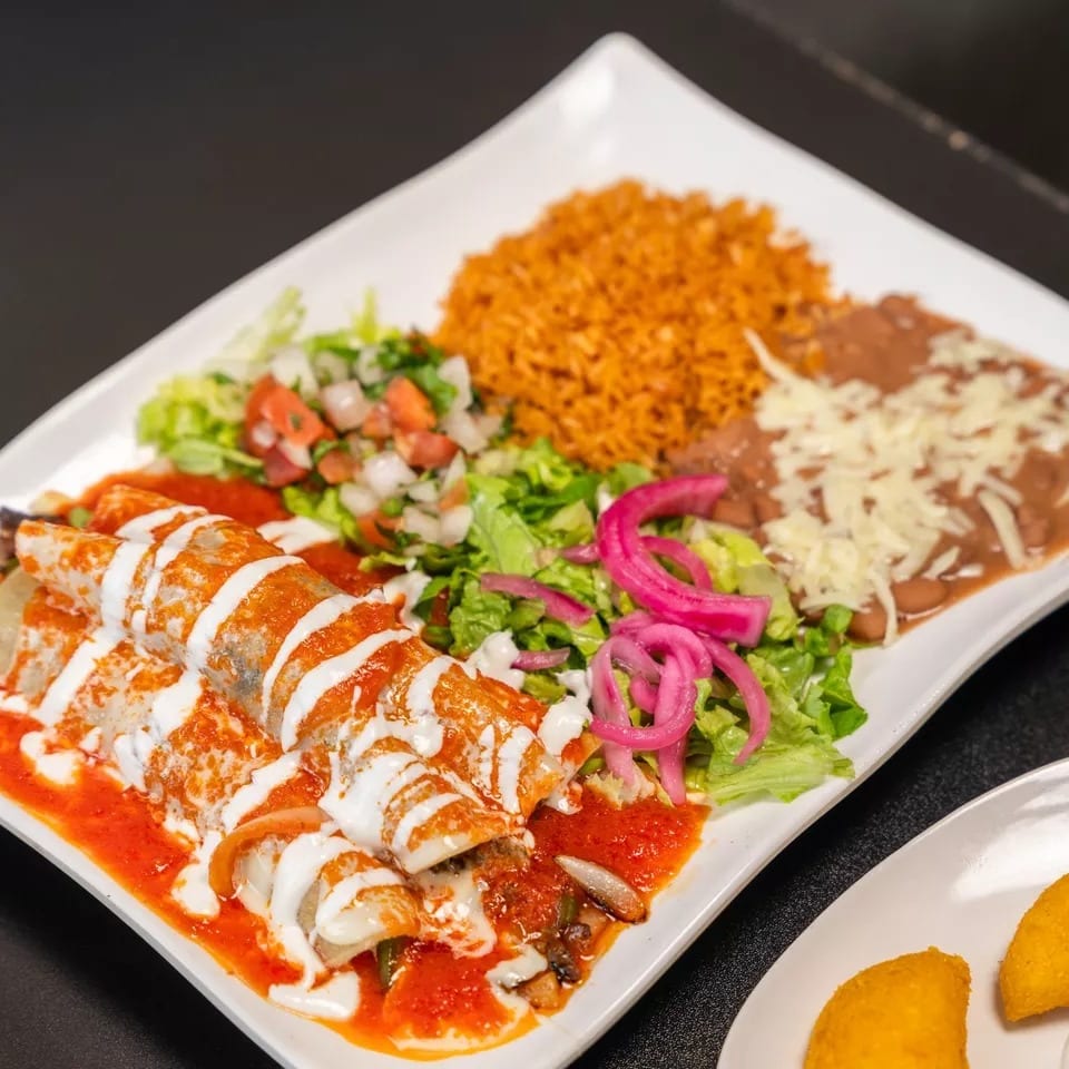 A plate of enchiladas with red sauce, crema, rice, beans, and a side salad.